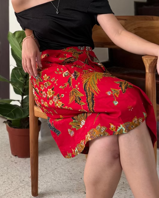 Woman sitting on a chair in a living room wearing a black top and red floral skirt.